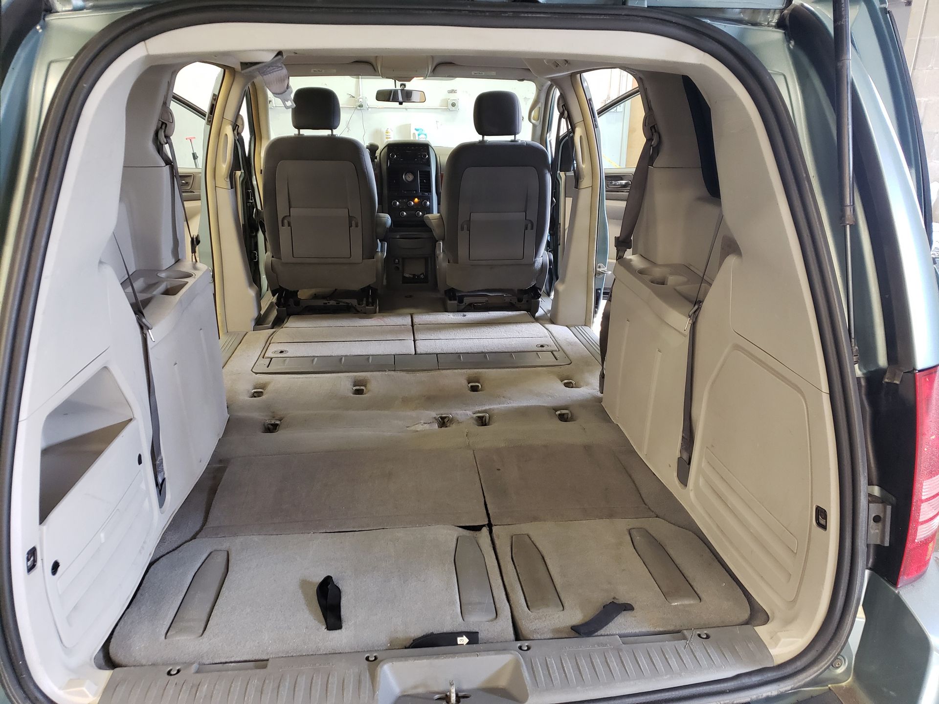 Empty minivan interior, showing the cargo area and second row seating. Gray and beige tones dominate.