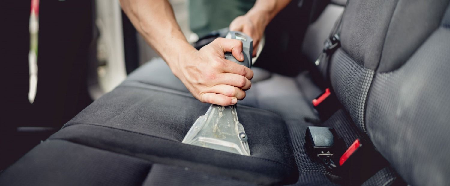 Person vacuuming a black car seat with a handheld vacuum.