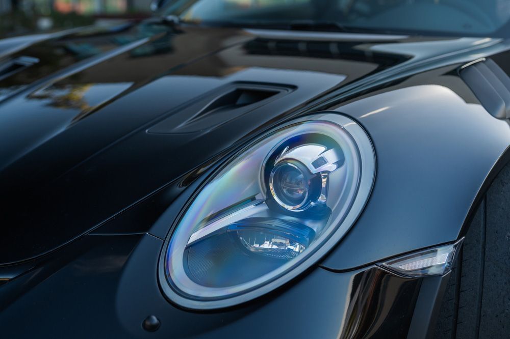 A close-up of the front headlight and hood vent of a sleek, black Porsche sports car.