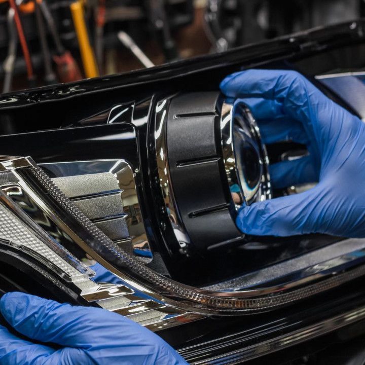 Hands in blue gloves holding a car headlight component, likely for installation or repair.