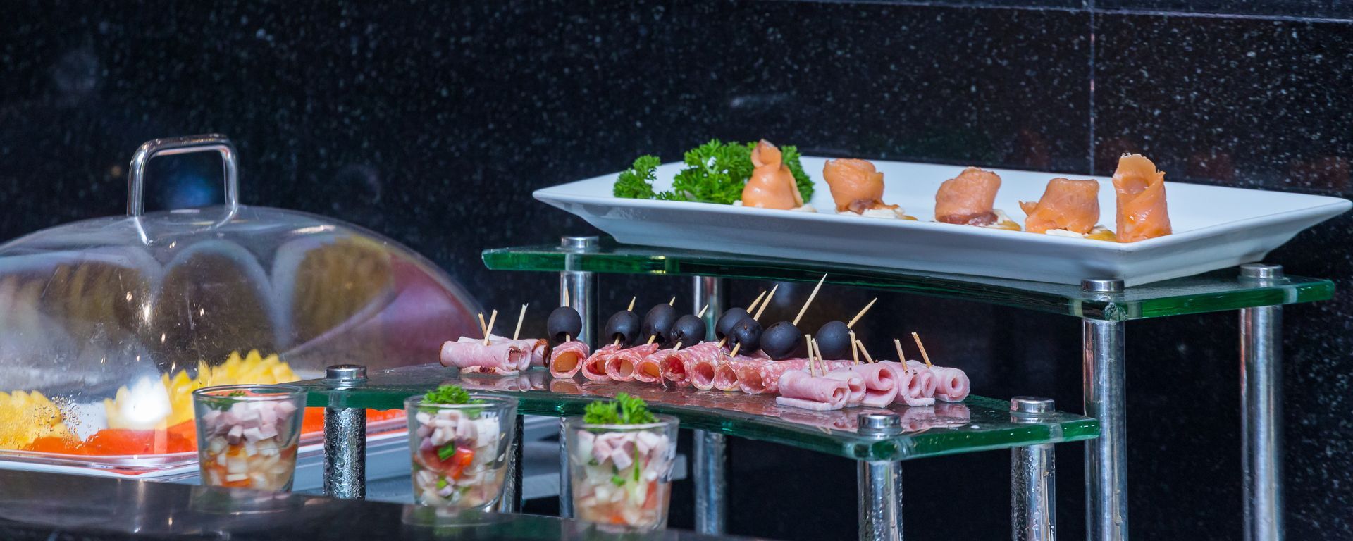 A buffet table with plates of food and a glass dome.