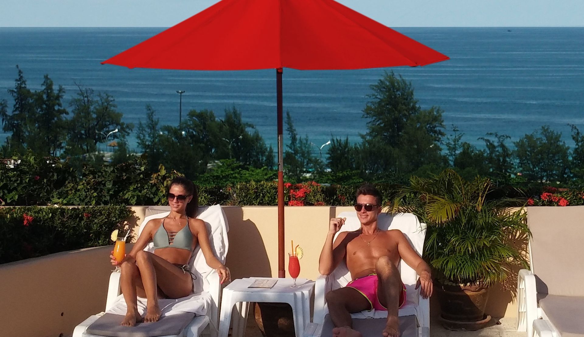 A man and a woman are sitting under an umbrella overlooking the ocean