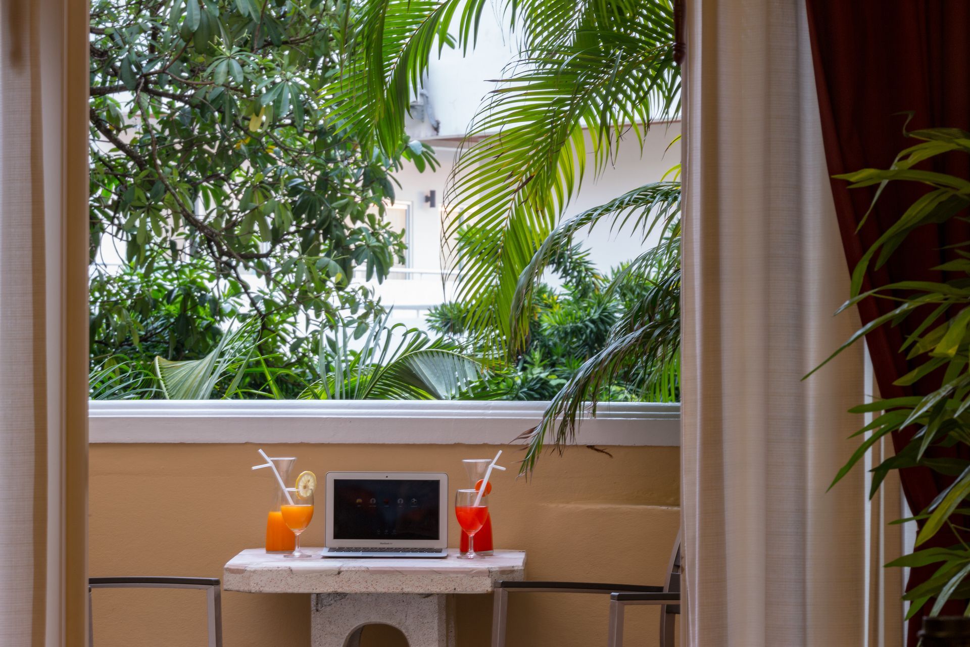 A table with a laptop and two drinks on it in front of a window.