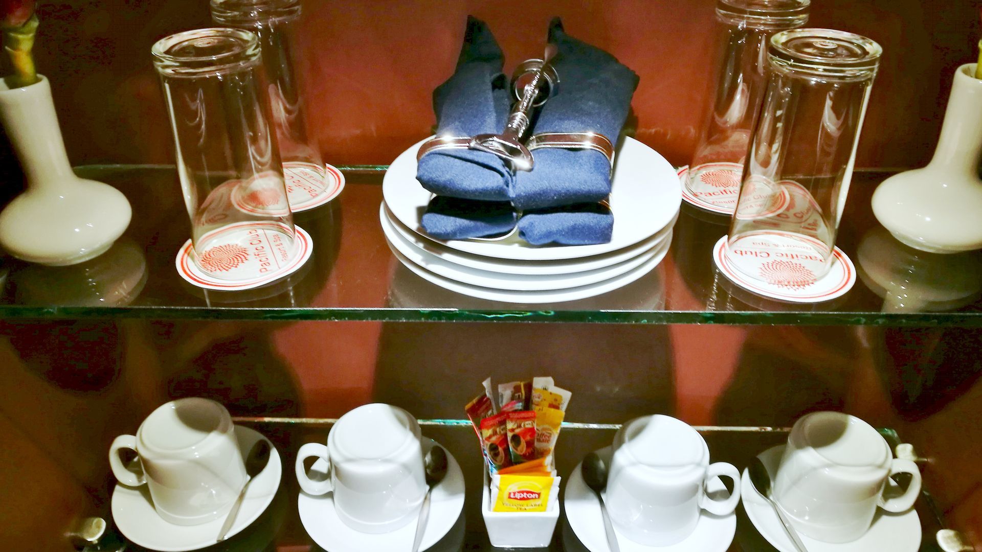 A glass shelf with cups saucers and glasses on it