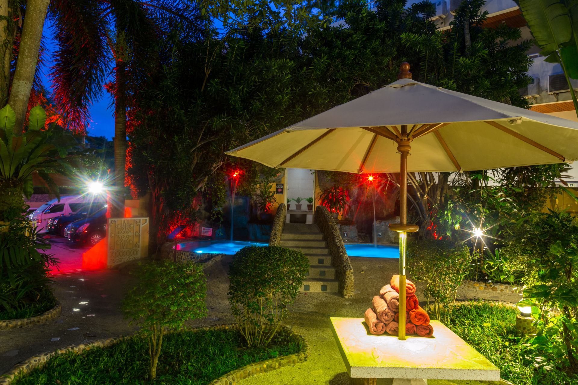 A white umbrella is sitting on a table in front of a swimming pool.