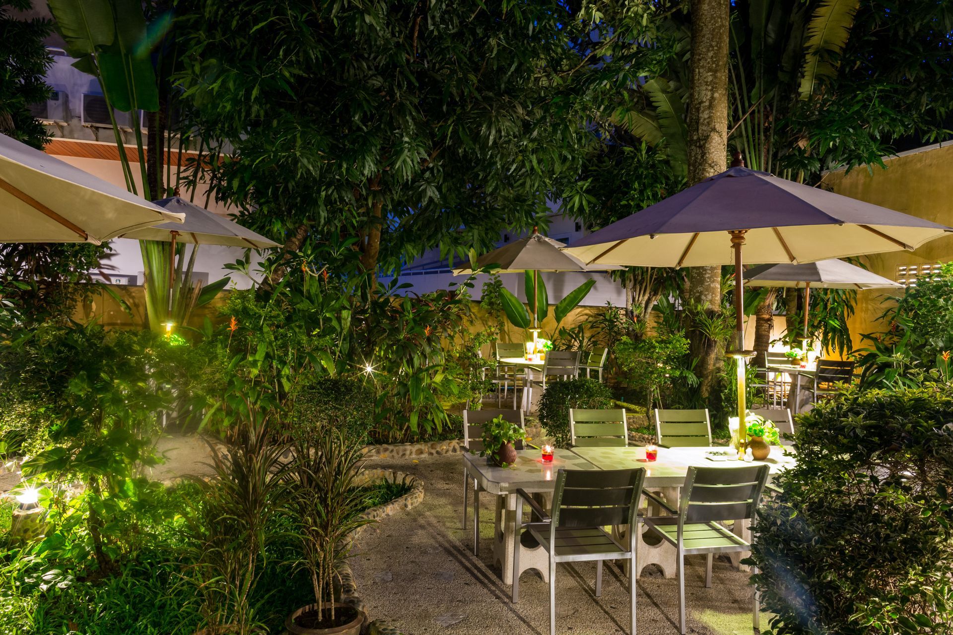 A garden with tables and chairs and umbrellas at night