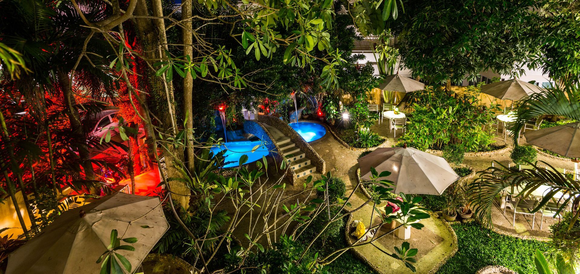 A swimming pool is surrounded by trees and umbrellas at night.