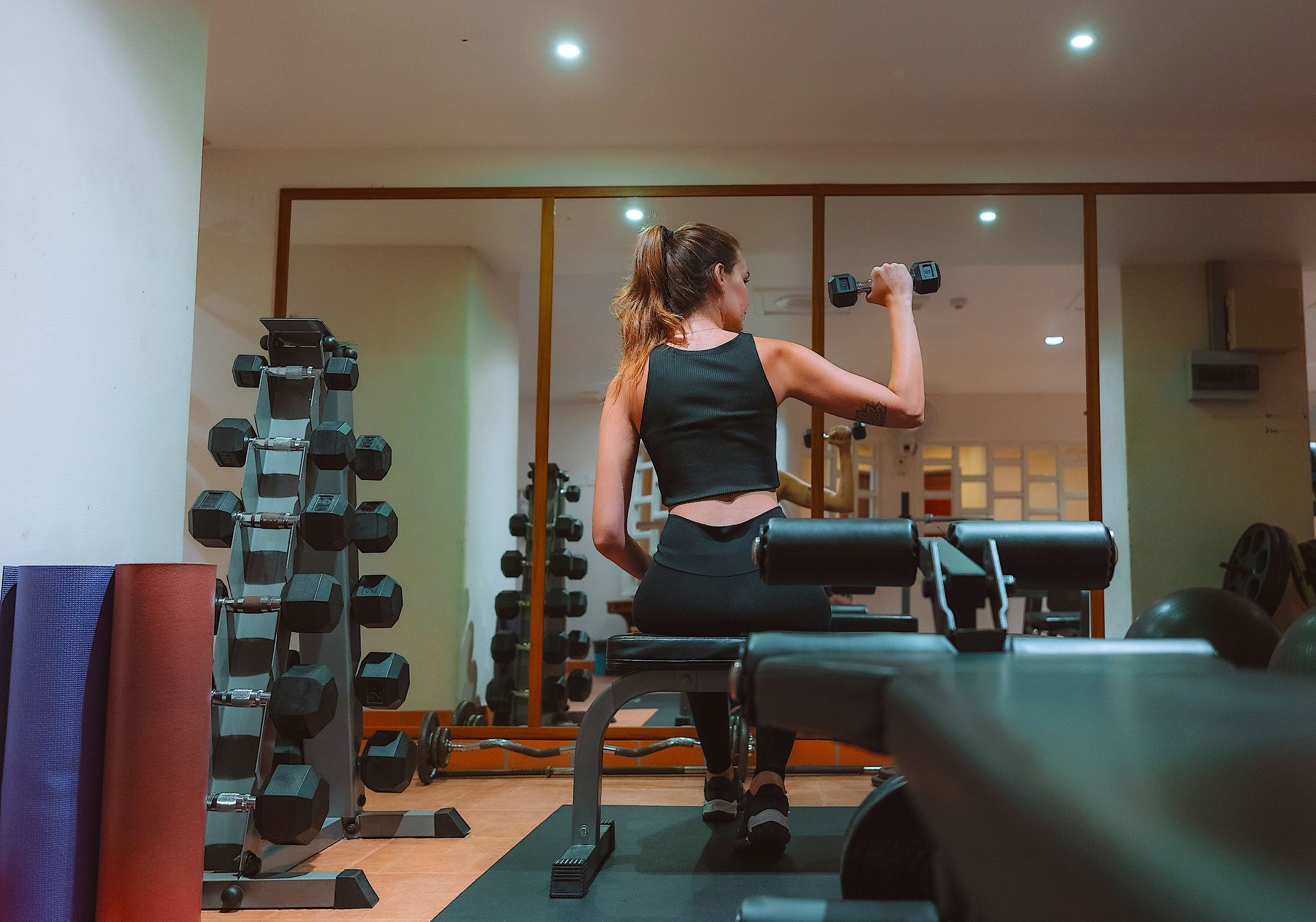 A woman is sitting on a bench in a gym holding a dumbbell.