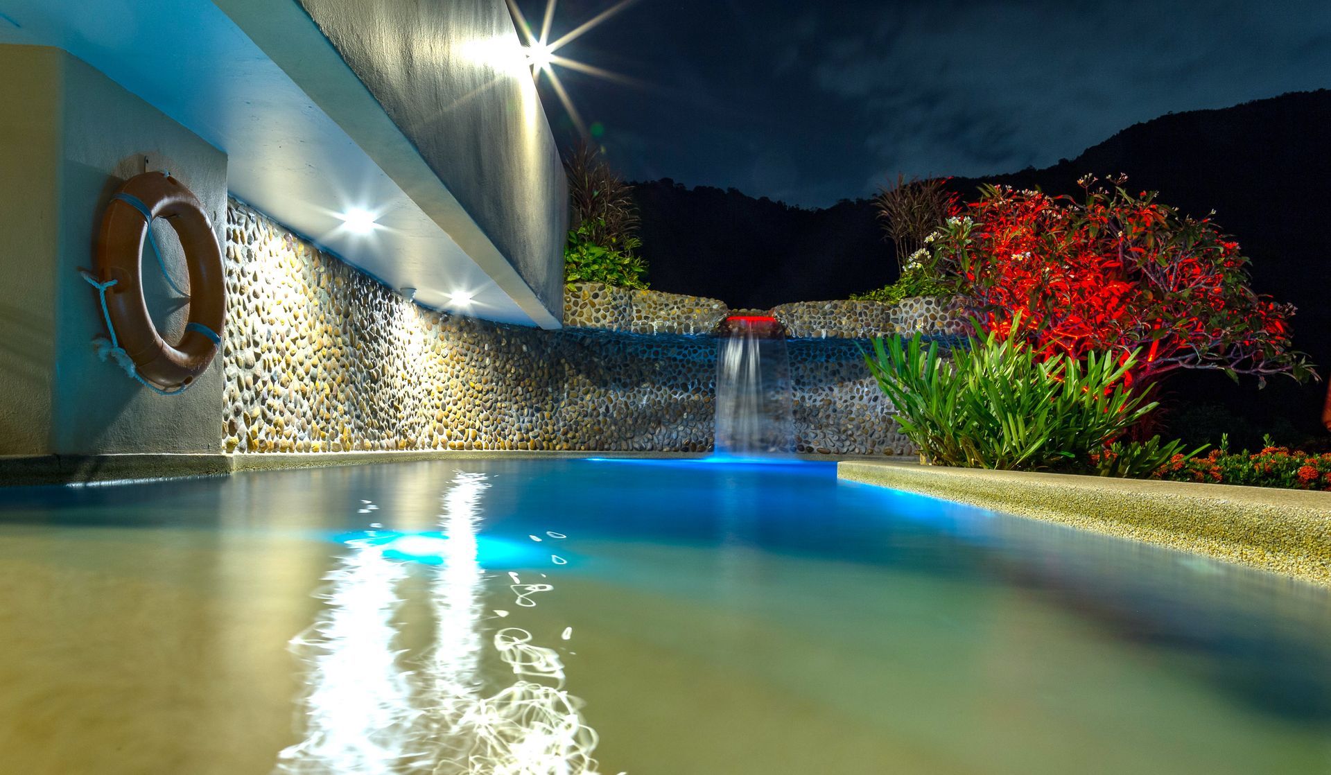 A large swimming pool with a waterfall in the background at night