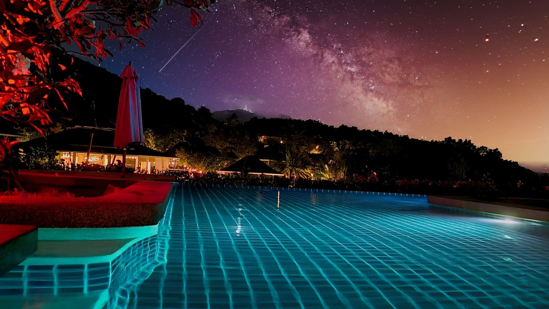 A swimming pool is lit up at night with a starry sky in the background.