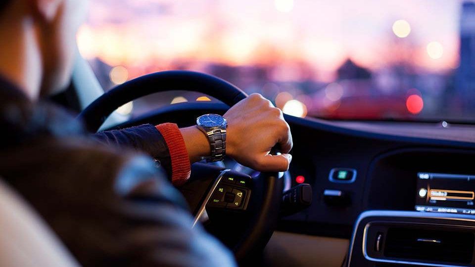 A man is driving a car at night with his hand on the steering wheel.