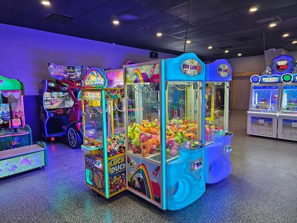 Arcade with claw machines and other games, lit with neon lights.