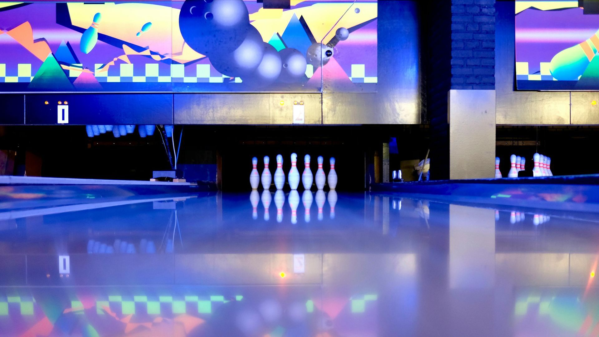Bowling lane with set of pins at the end; illuminated with blue and neon colors.