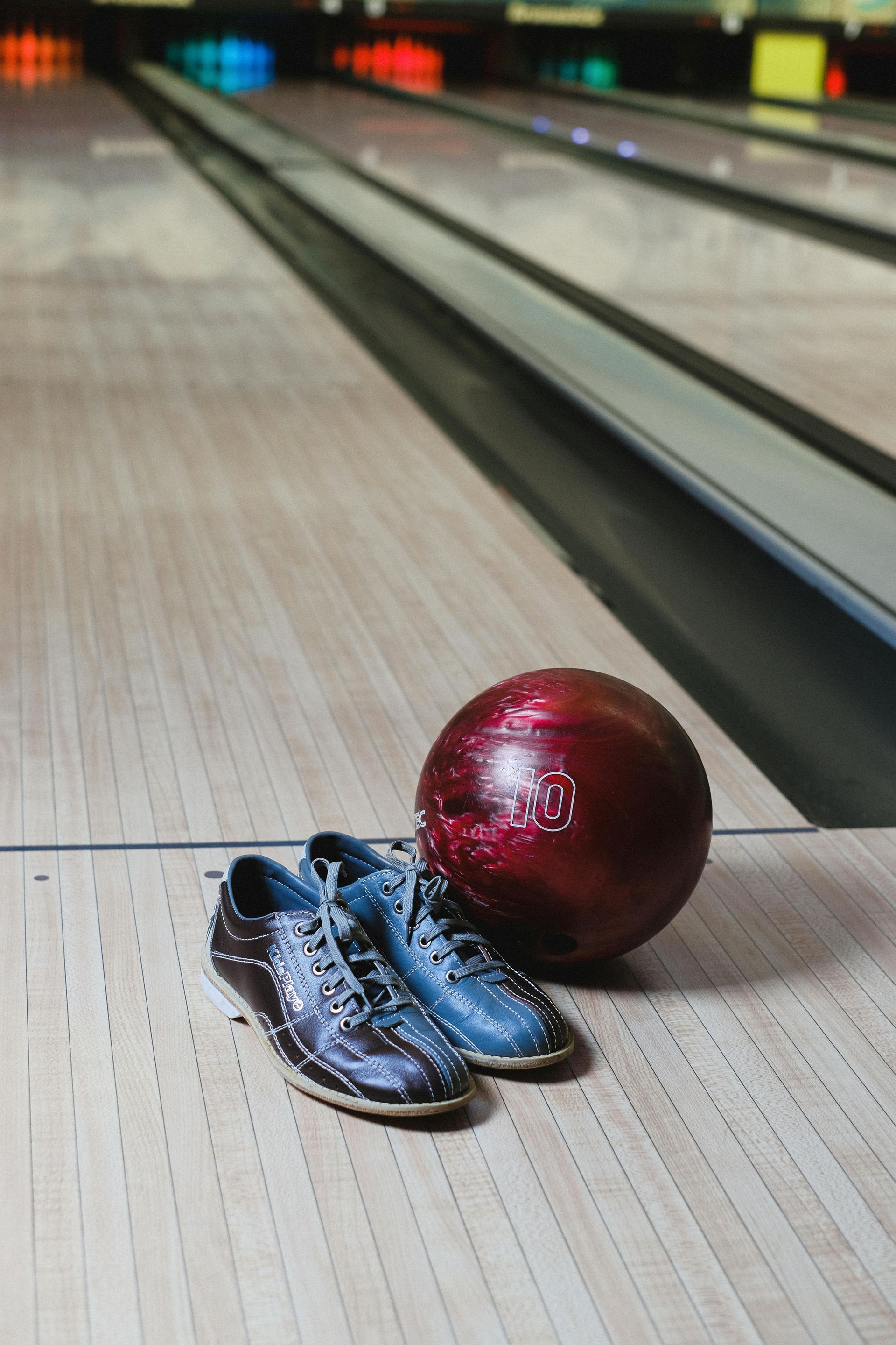 Bowling ball and shoes on a wooden lane; the background shows multiple lanes.