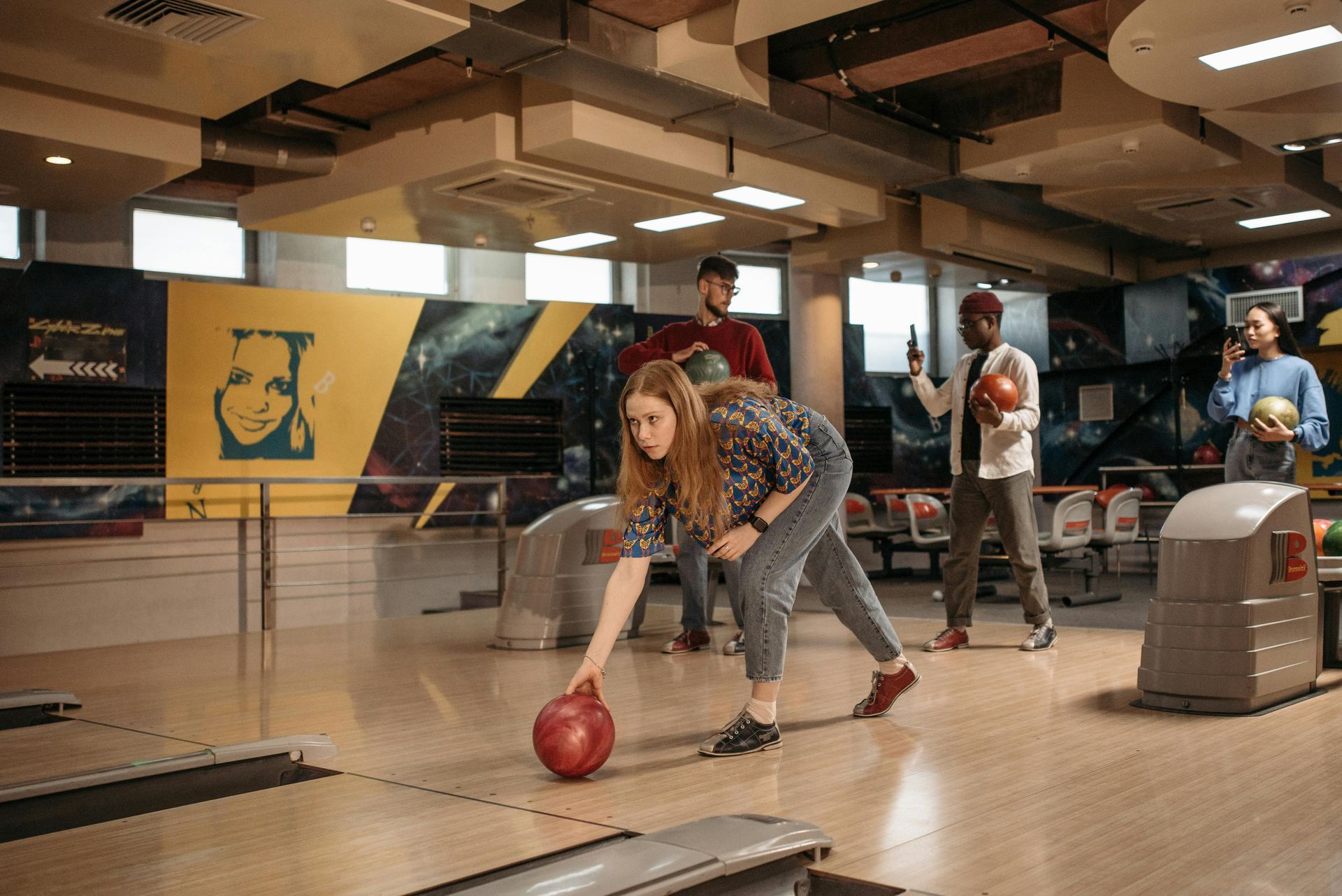 Woman bowling, aiming the ball down the lane, with friends watching in a bowling alley.