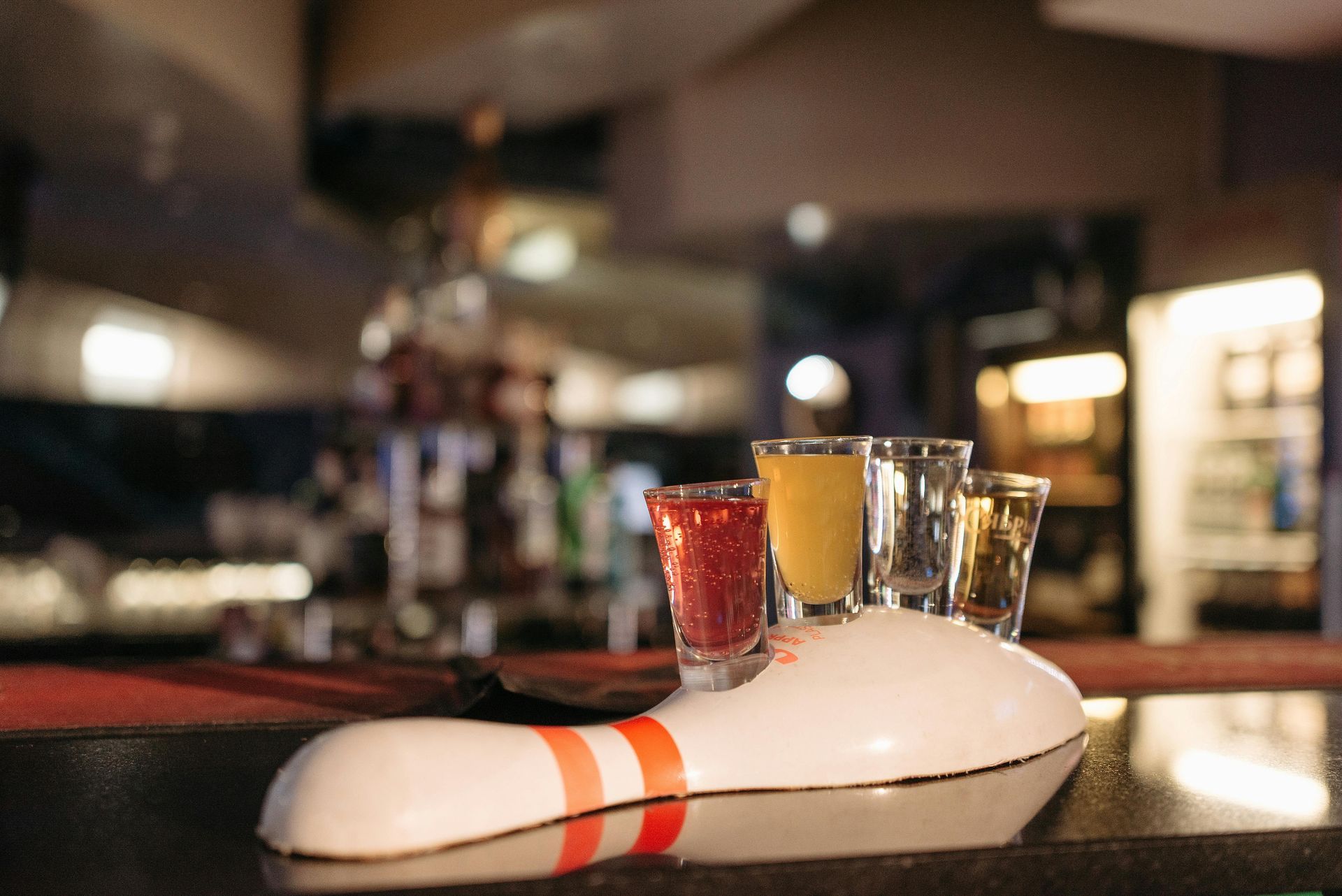 Shot glasses filled with colorful drinks on a bowling pin-shaped holder, bar background.