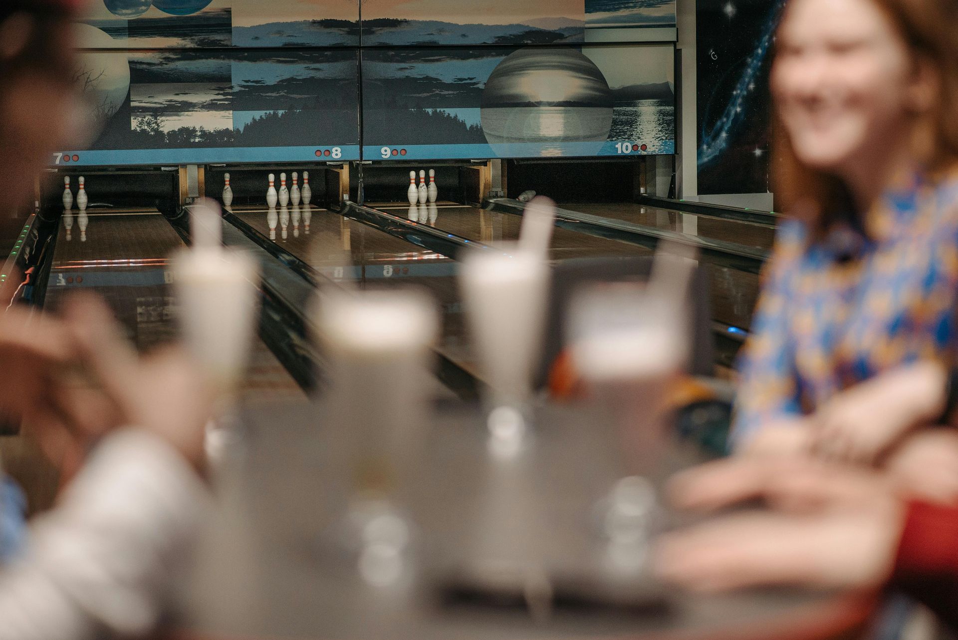 Bowling alley with pins at the end of the lane. People are blurred in the foreground around drinks.
