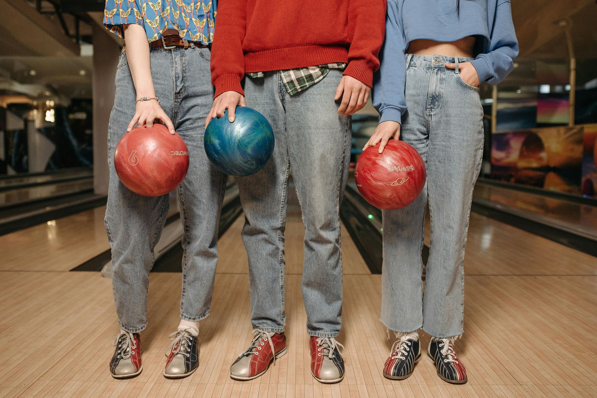 Three people holding bowling balls in a bowling alley.