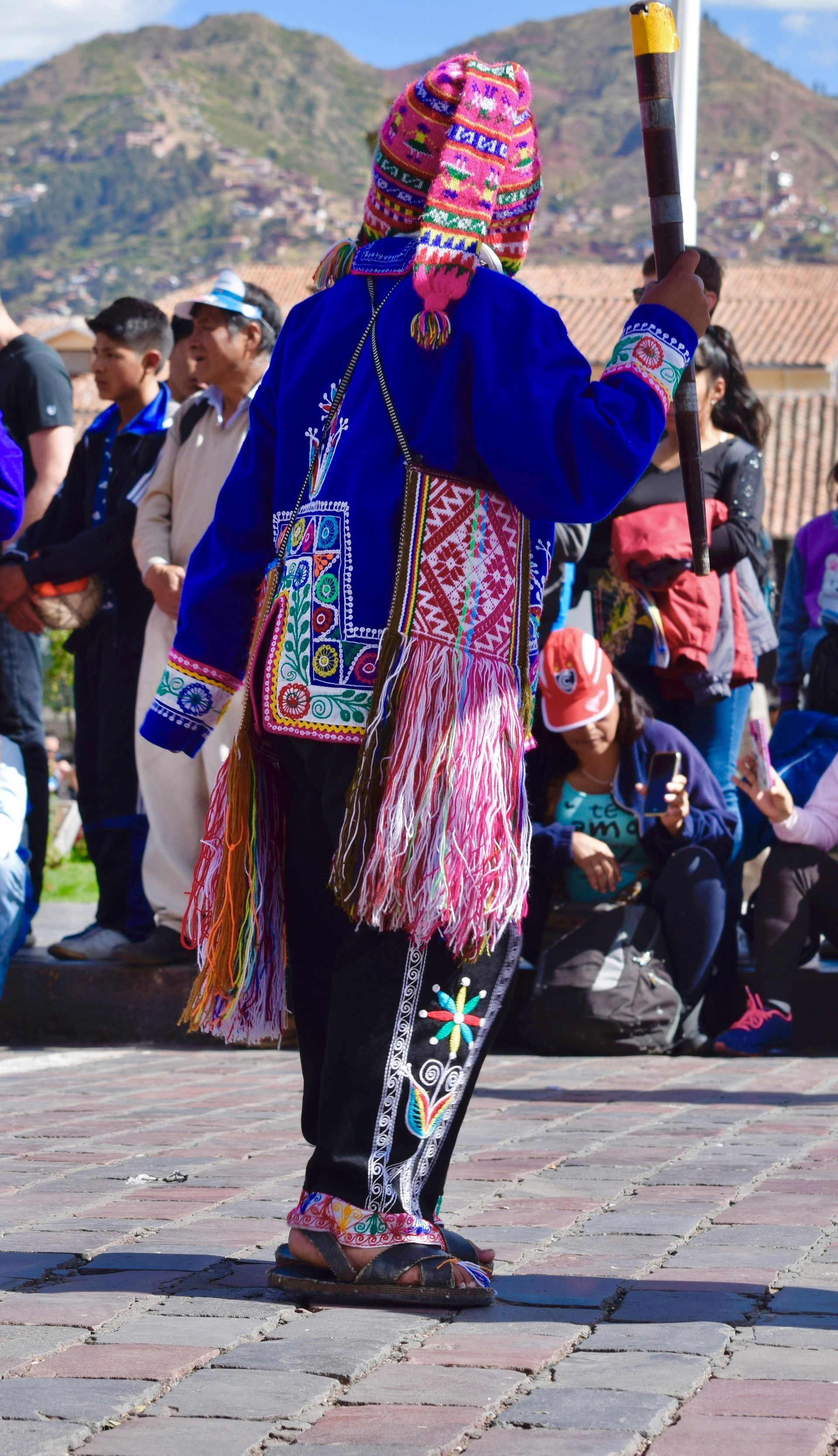 Un artista ataviado con vestimenta andina tradicional, que incluye un gorro colorido, una chaqueta azul y textiles bordados.