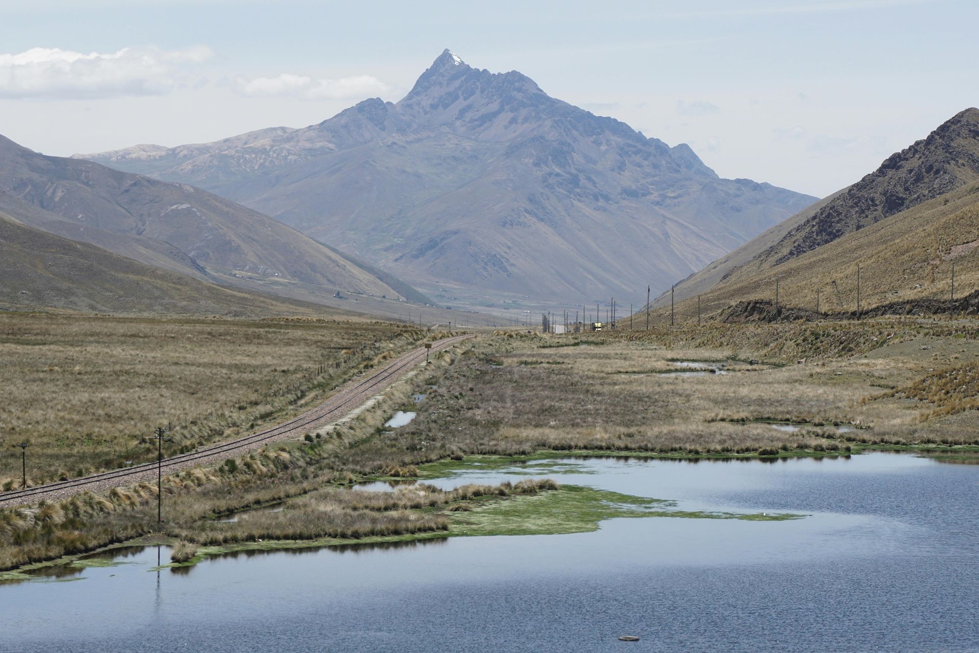 Un lago en primer plano conduce a un camino de tierra que serpentea a través de un valle montañoso y cubierto de hierba.