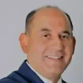 Man with fair skin, smiling, wearing a dark blue suit jacket.