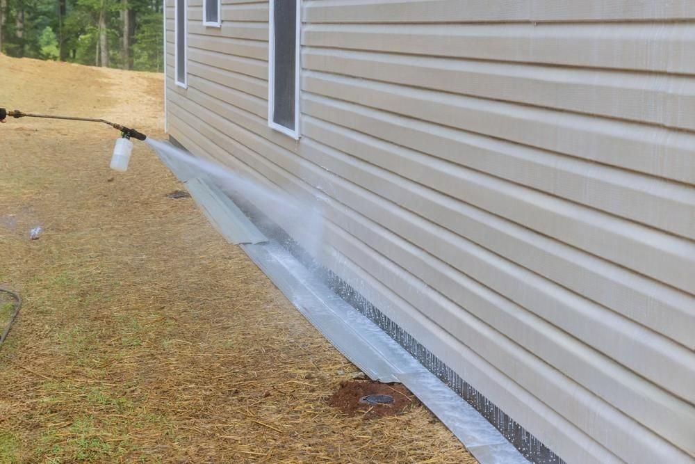 A person is spraying water on the side of a house.