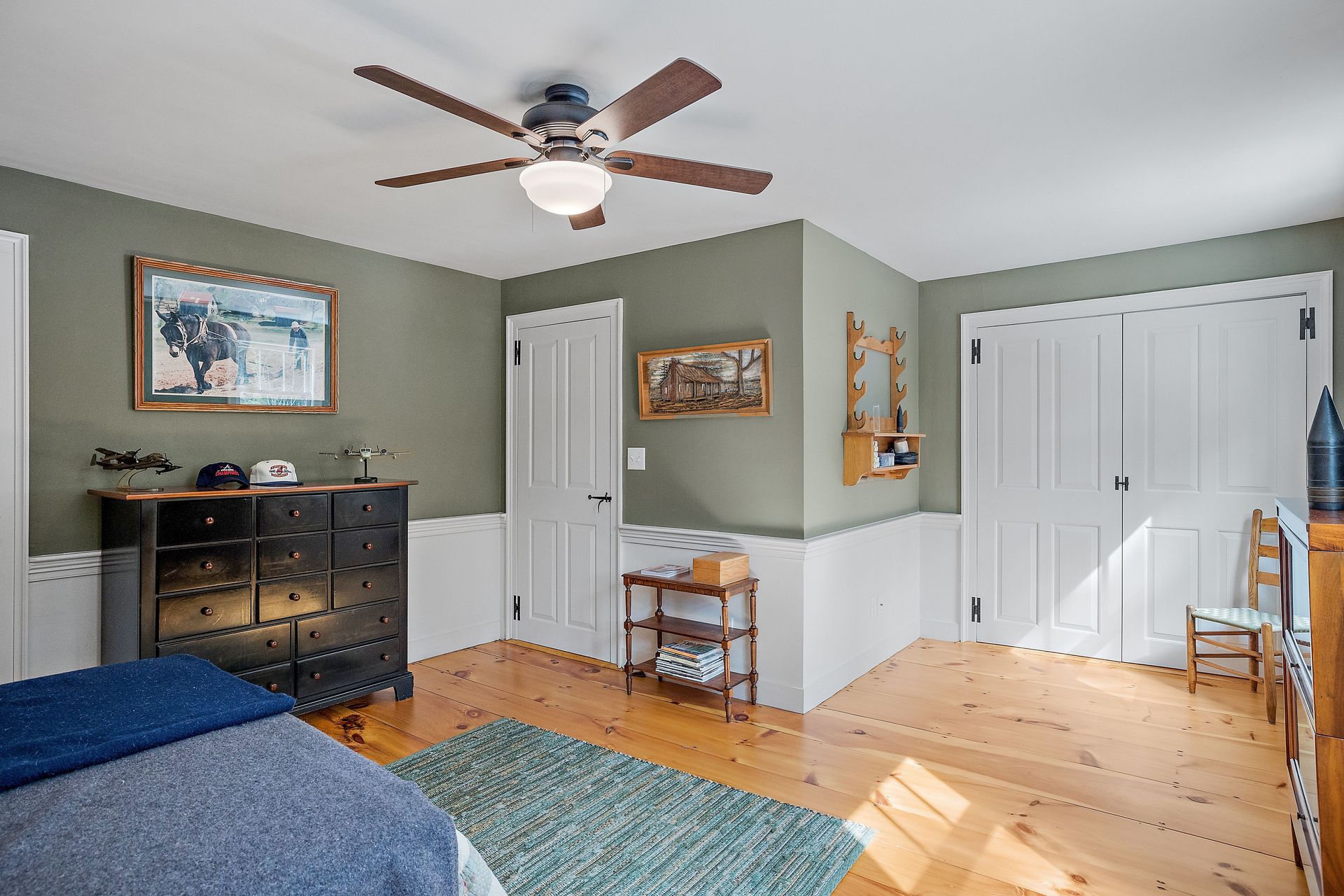 Bedroom with sage green walls, white trim, wood floors, dark dresser, and ceiling fan.