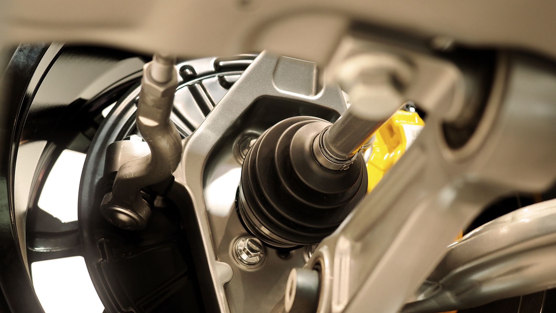 Close-up view of car suspension components: axle, brake, and steering linkage.