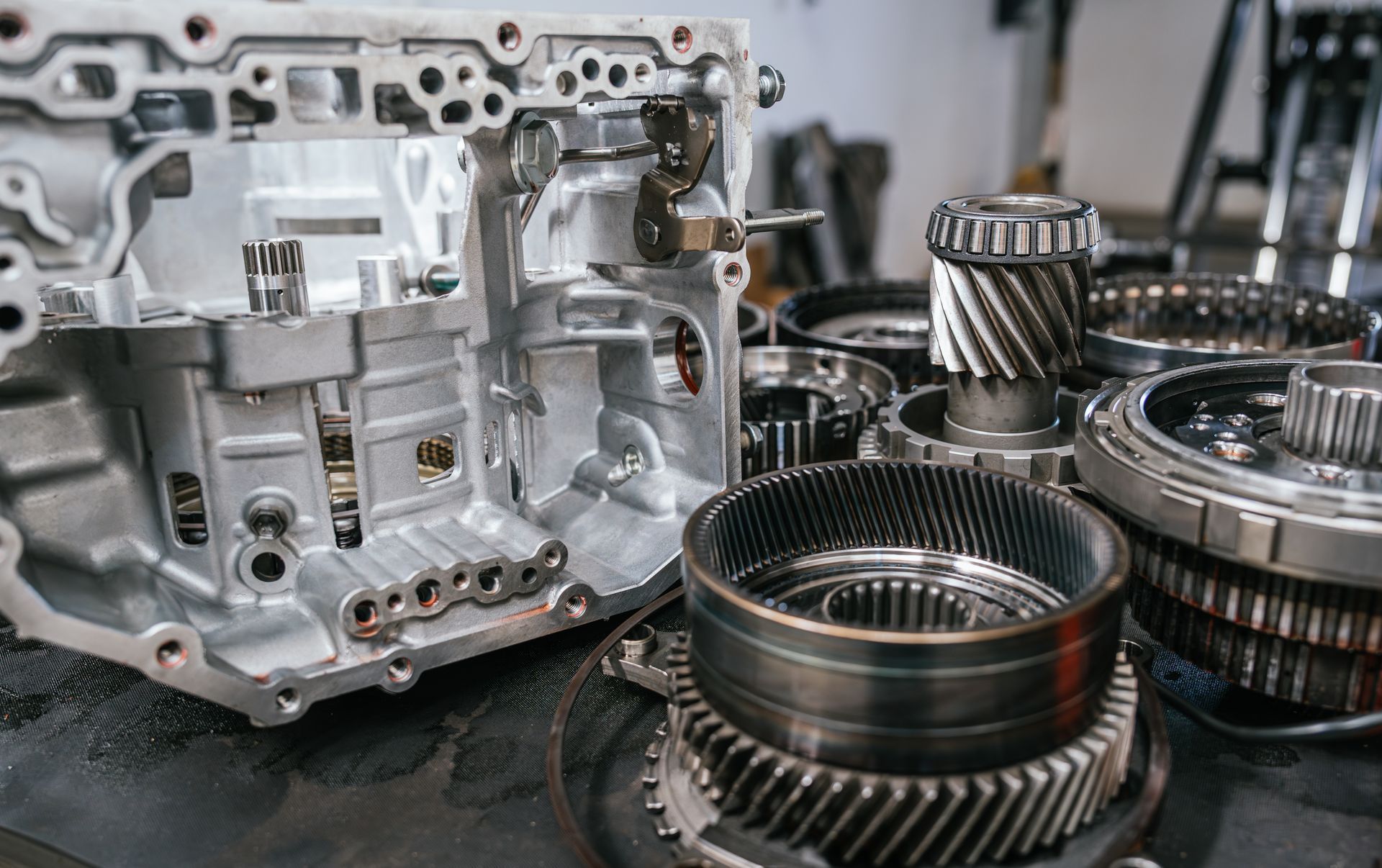 Disassembled car transmission with metal gears and housing parts, in a workshop setting.