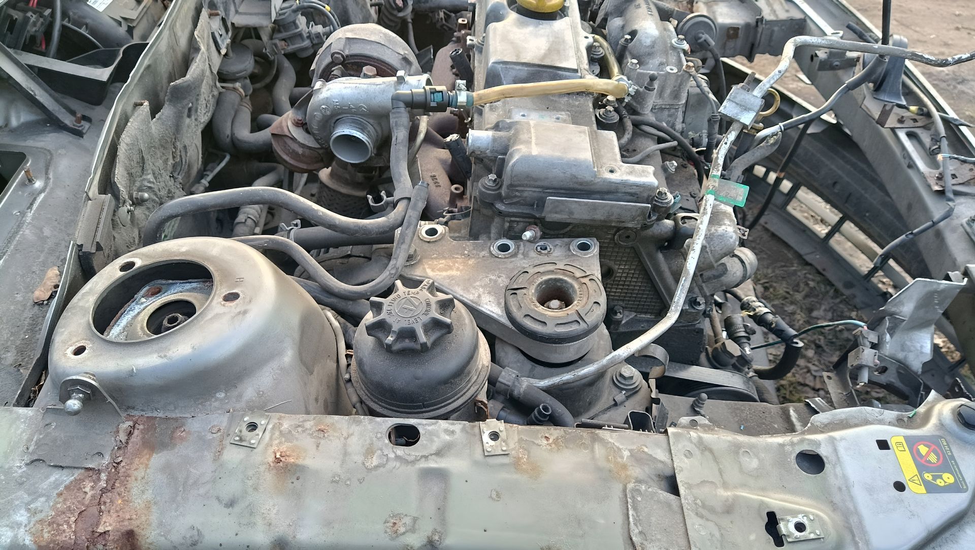 Charred car engine bay with burnt hoses and melted components, showing severe fire damage