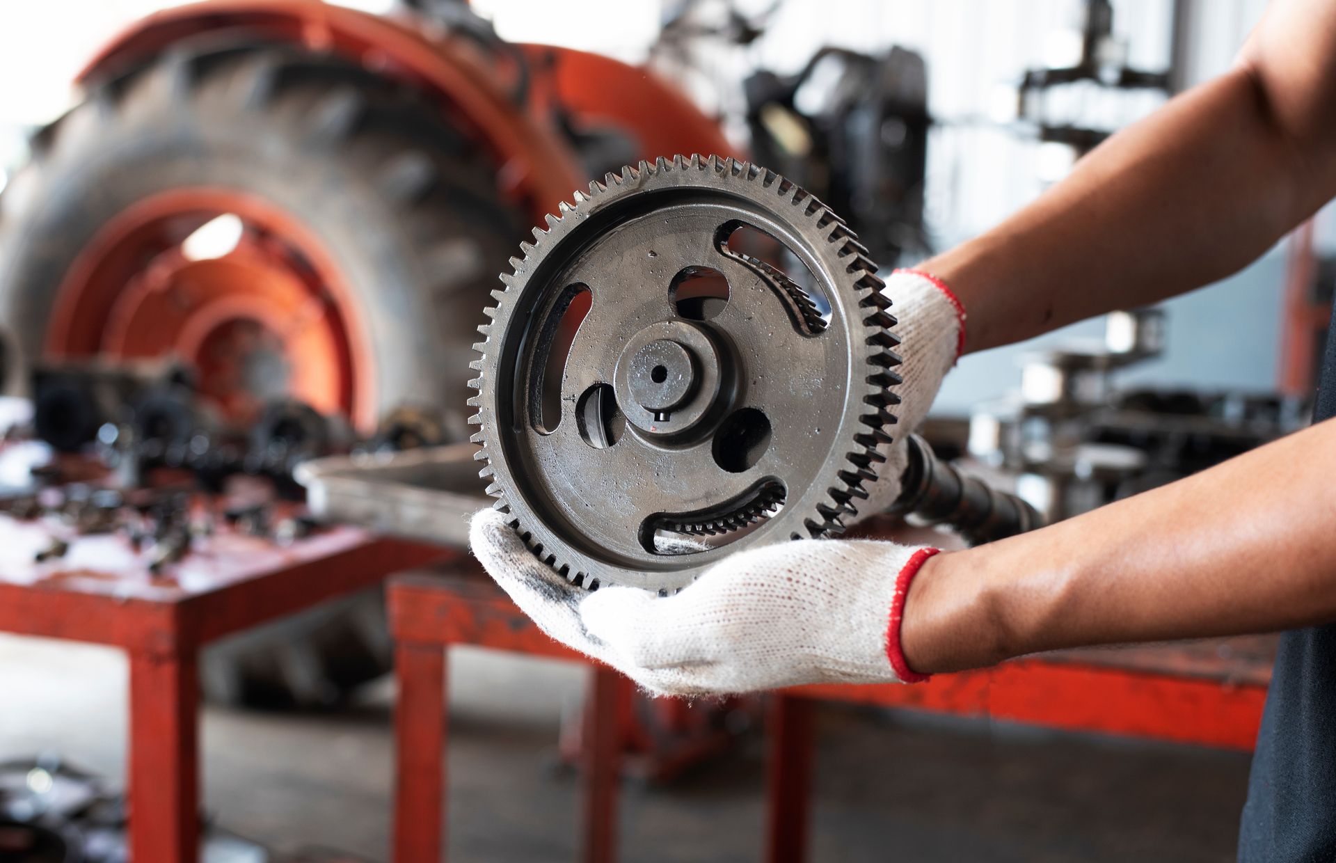 Mechanic holding a gear, with tractor and worktable in the background.