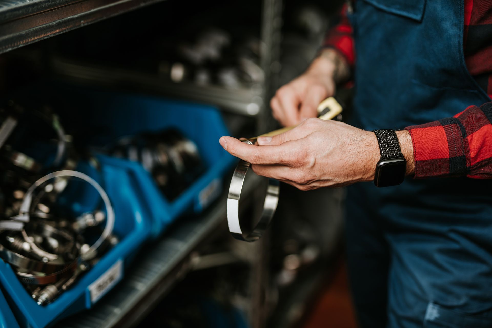 A person in overalls and a red plaid shirt holding a metal clamp in a storage area.