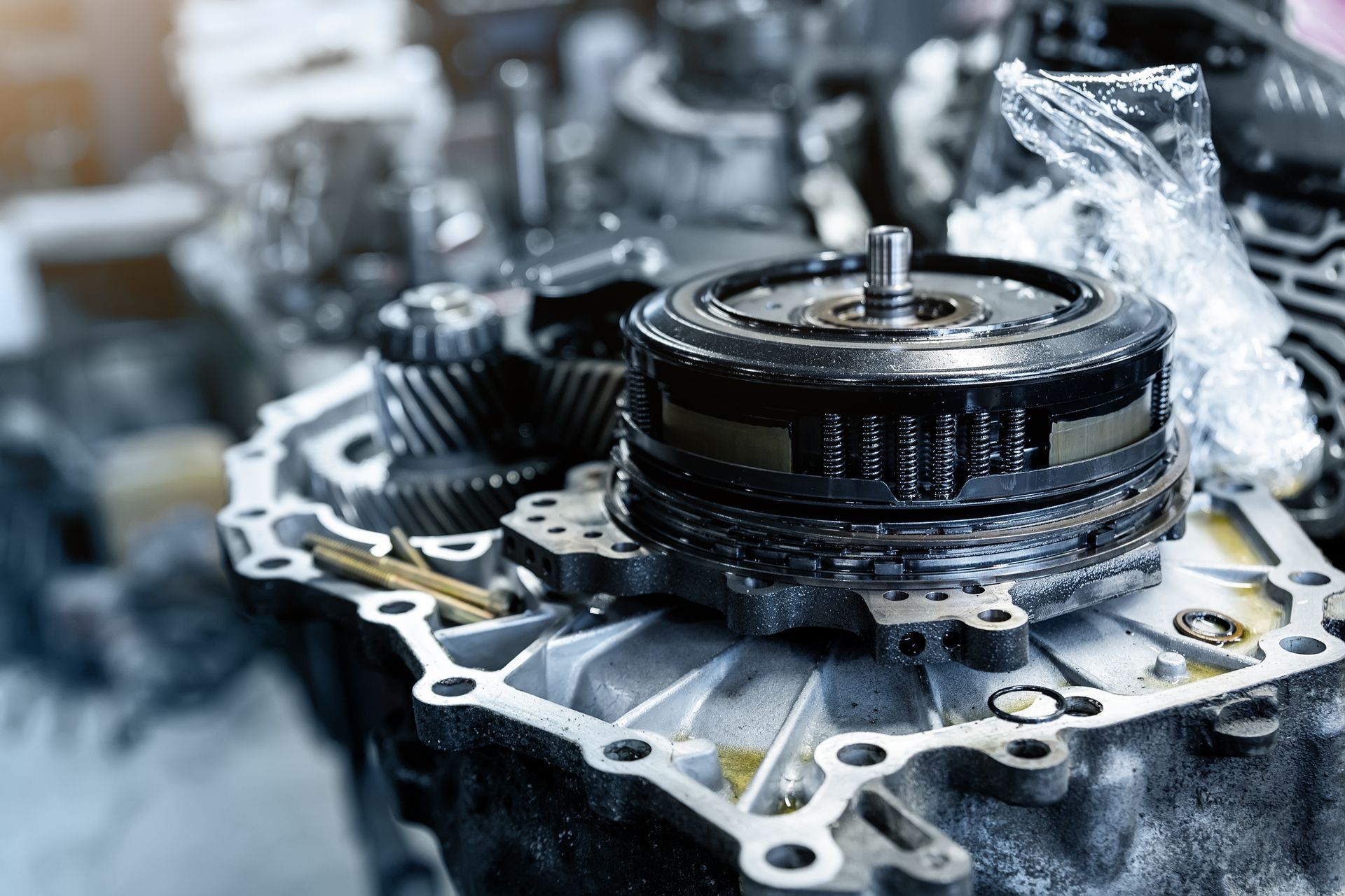 Disassembled car transmission parts, including gears and a torque converter, in a repair setting.
