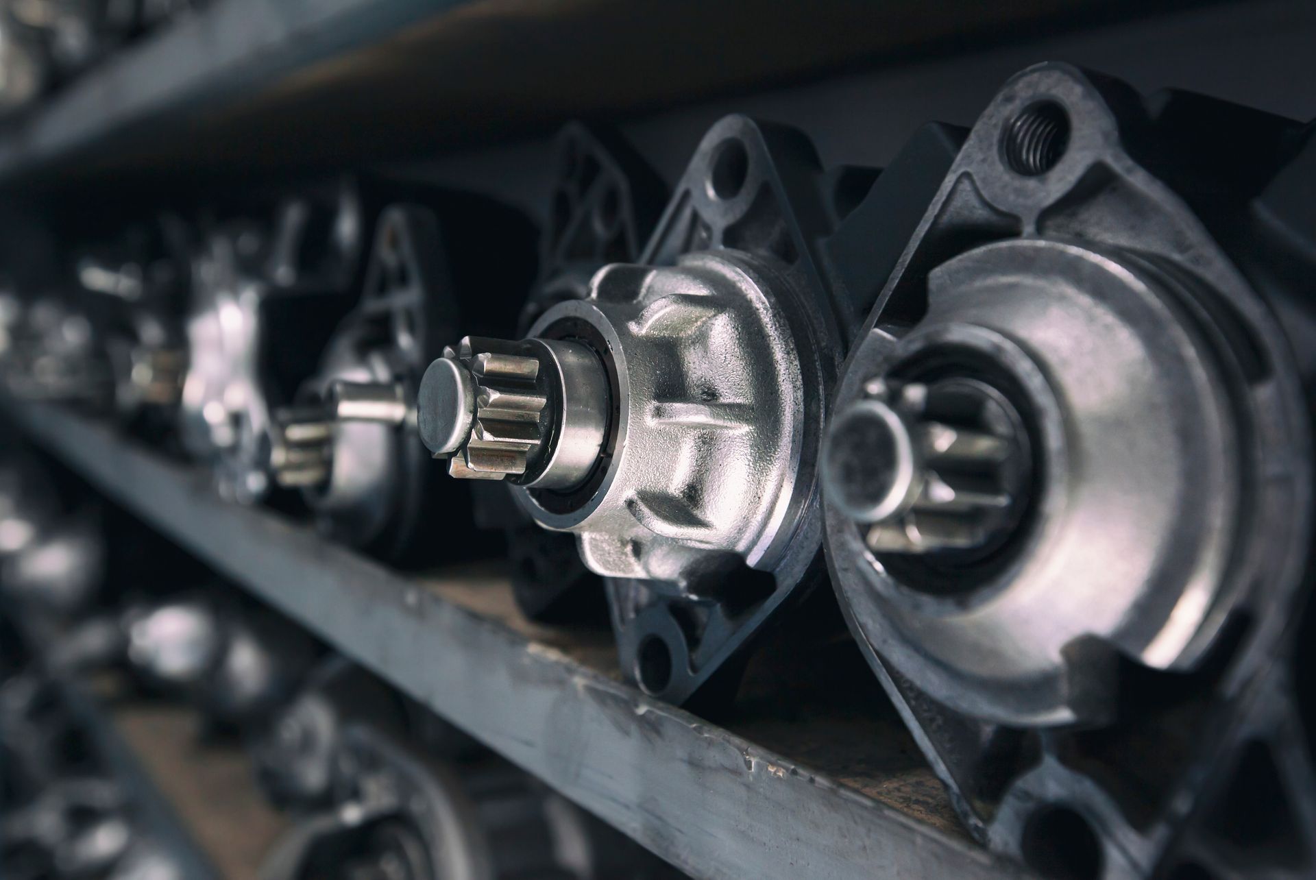 Automotive starters on a metal shelf, with visible gears and mounting flanges.