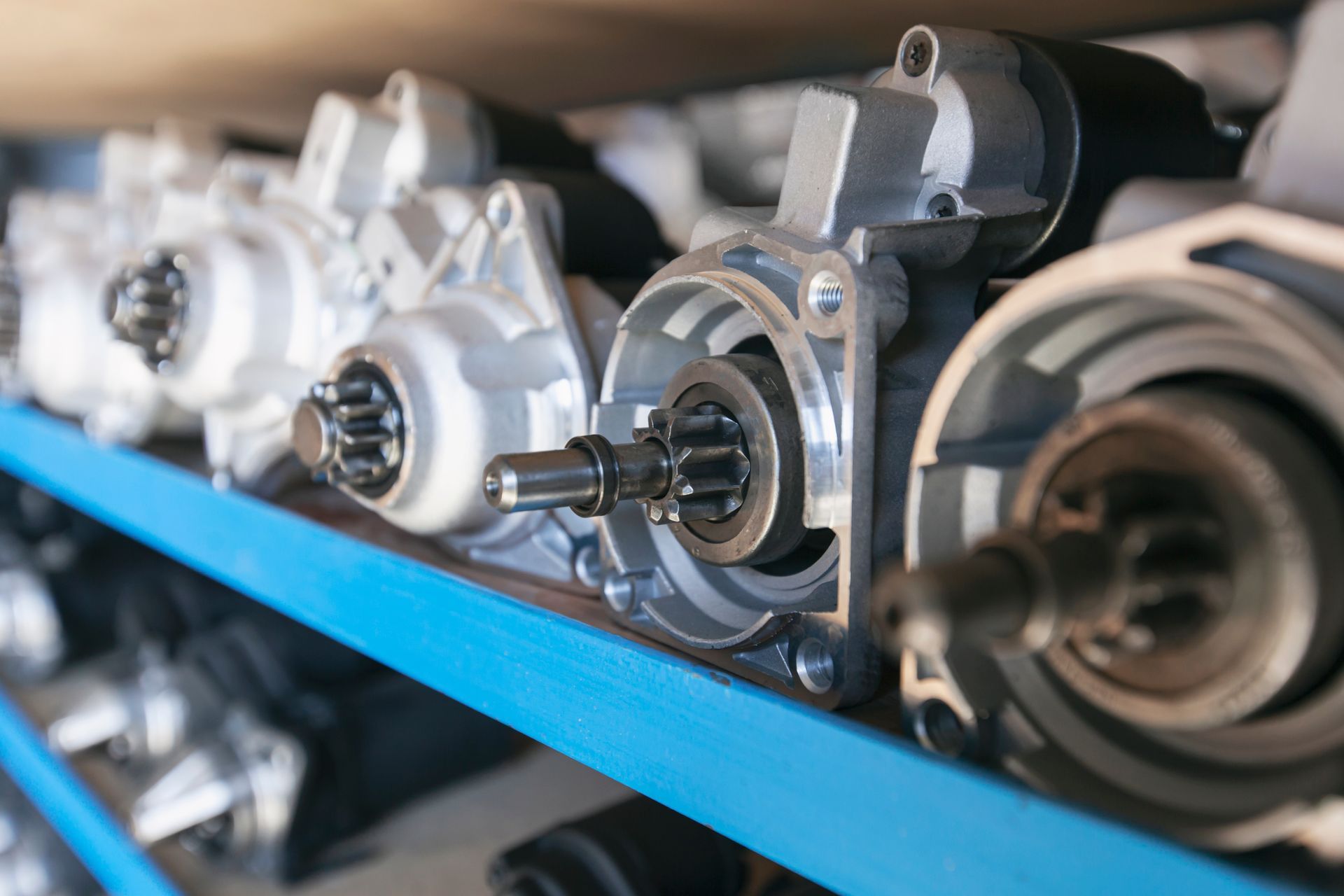 Car starters on a blue shelf, lined up inside a storage room.