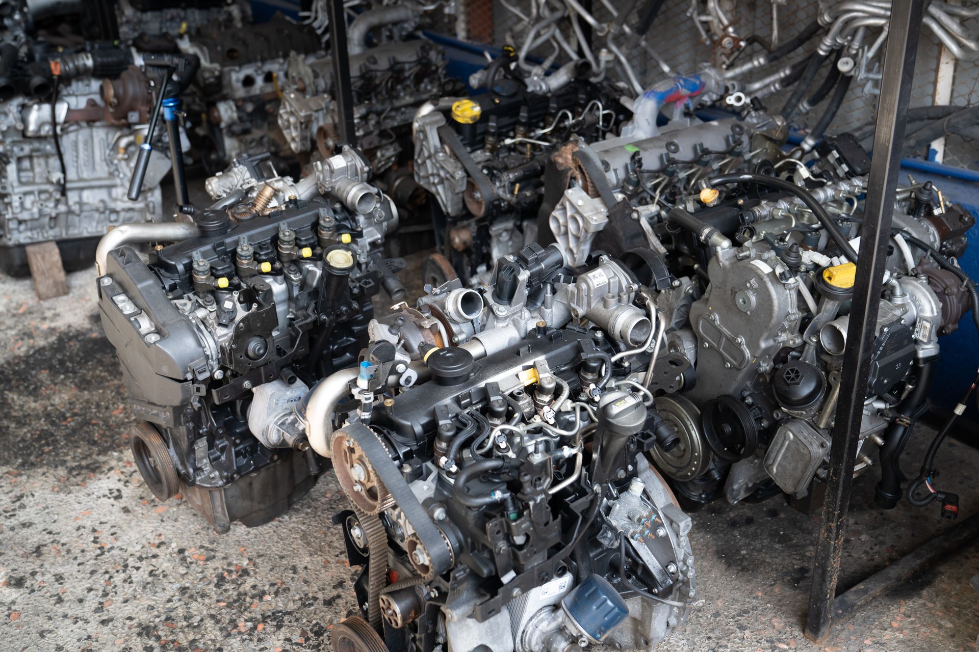 Pile of used car engines in a repair shop, various models, dark colors, some metal.
