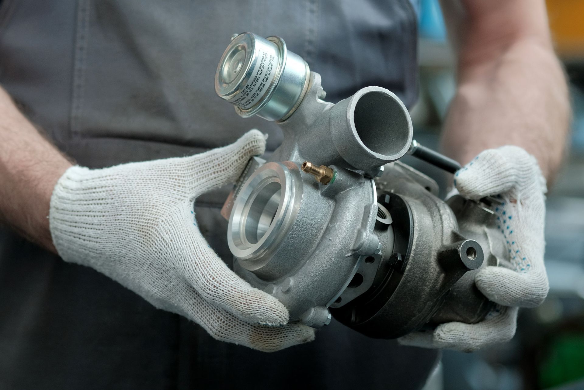 Hands in white gloves holding a metal turbocharger.