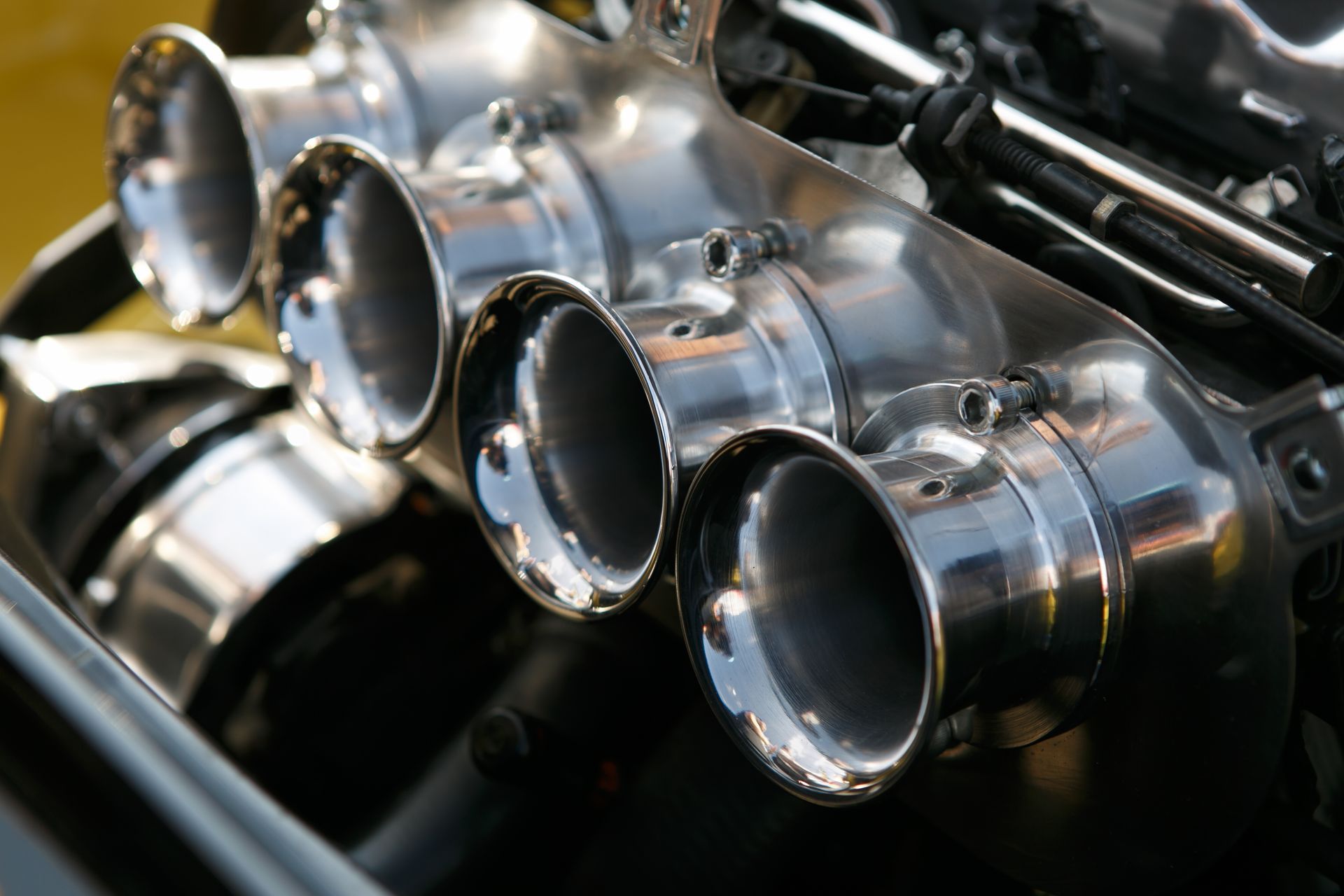 Polished intake manifold with four flared velocity stacks on a vehicle engine.