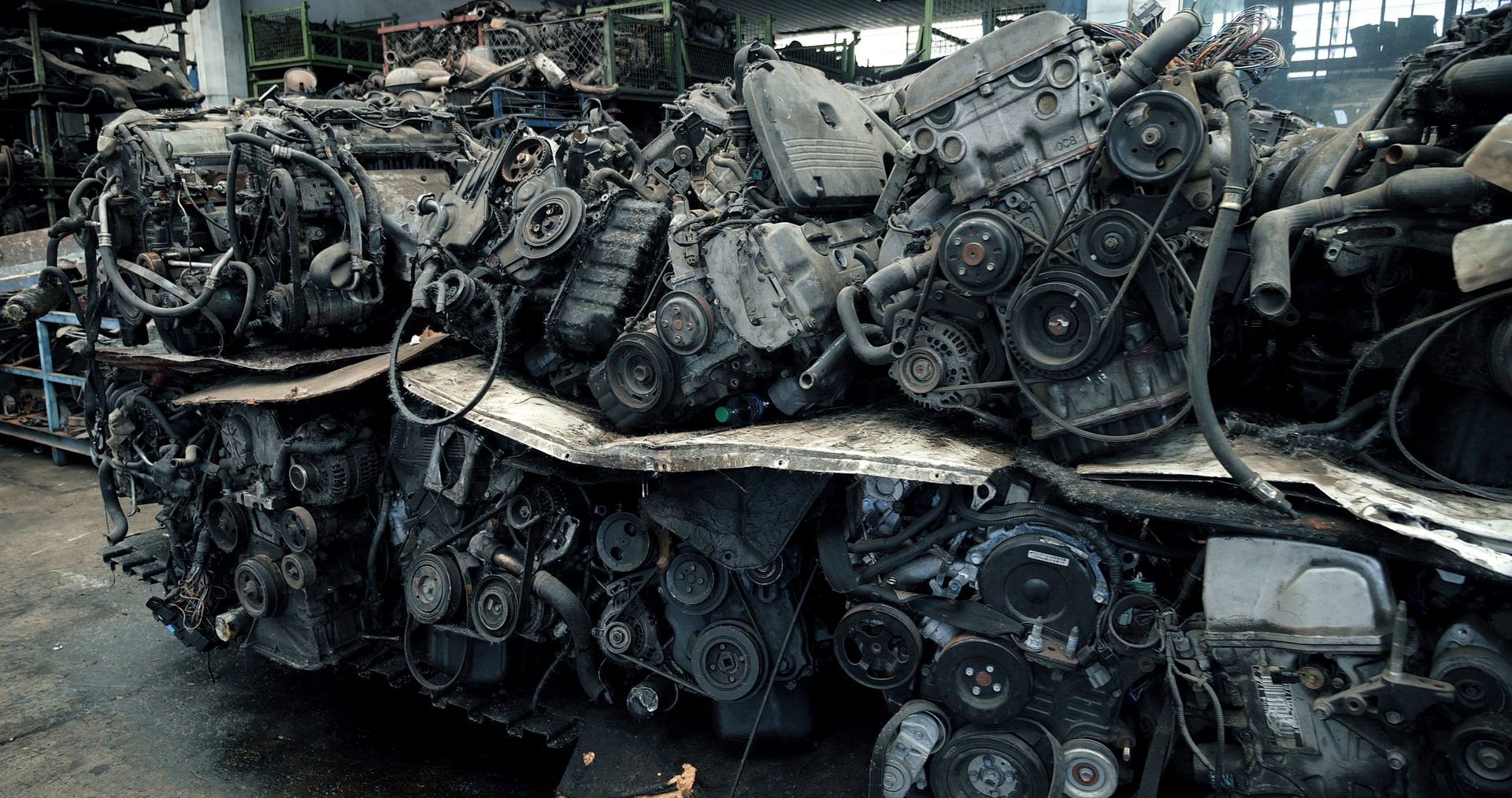 Pile of discarded car engines in a scrap yard, showing various mechanical components.