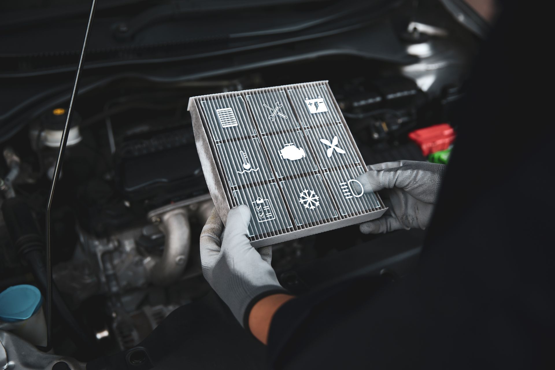 A mechanic holding a dirty cabin air filter in front of a car engine.