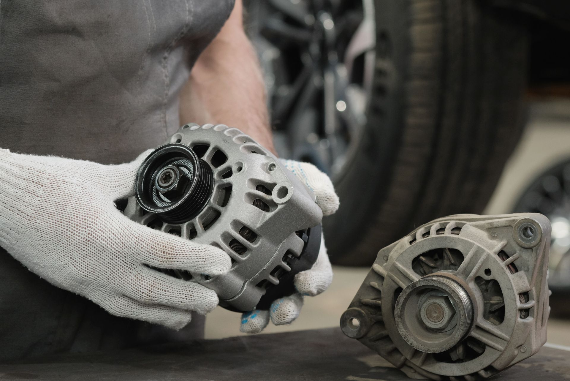 Mechanic holding a new alternator next to an old one, likely for comparison during replacement.