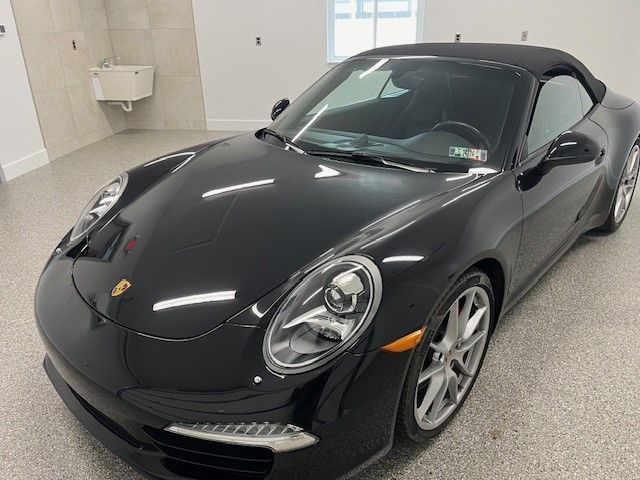 A black porsche 911 convertible is parked in a garage.