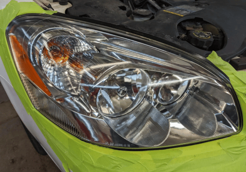 Close-up of a vehicle headlight masked with painter's tape