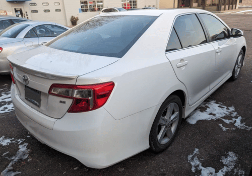 Rear three-quarter view of a white Toyota Camry sedan parked outdoors on a winter day