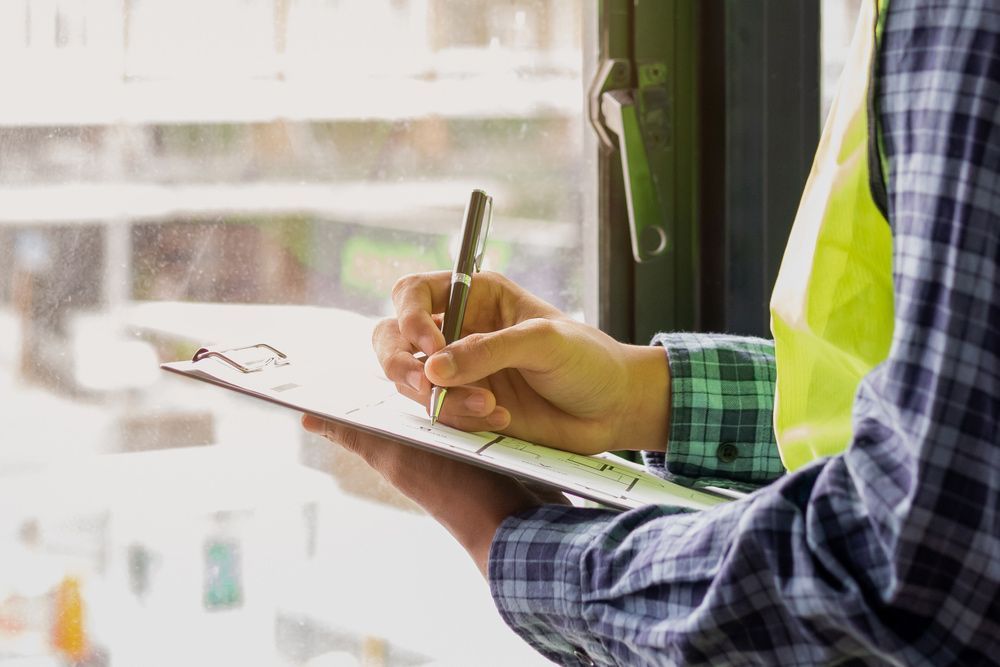 A Man Is Writing on A Clipboard in Front of A Window — Hager Surveying In Banora Point, NSW