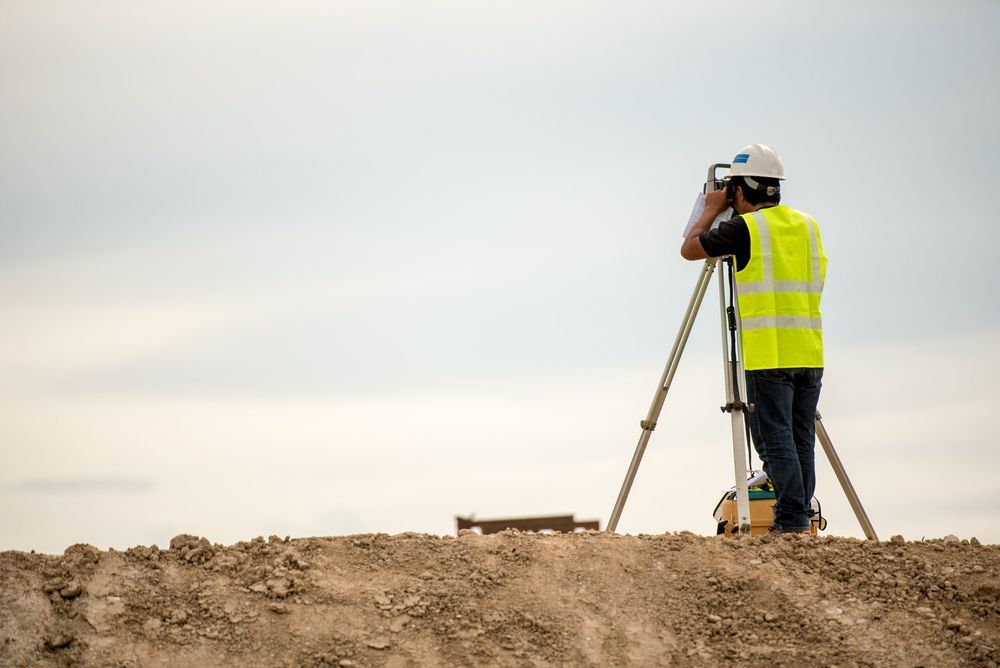 A Man Is Standing on Top of A Dirt Hill Looking Through a Telescope — Hager Surveying In Ballina, NSW