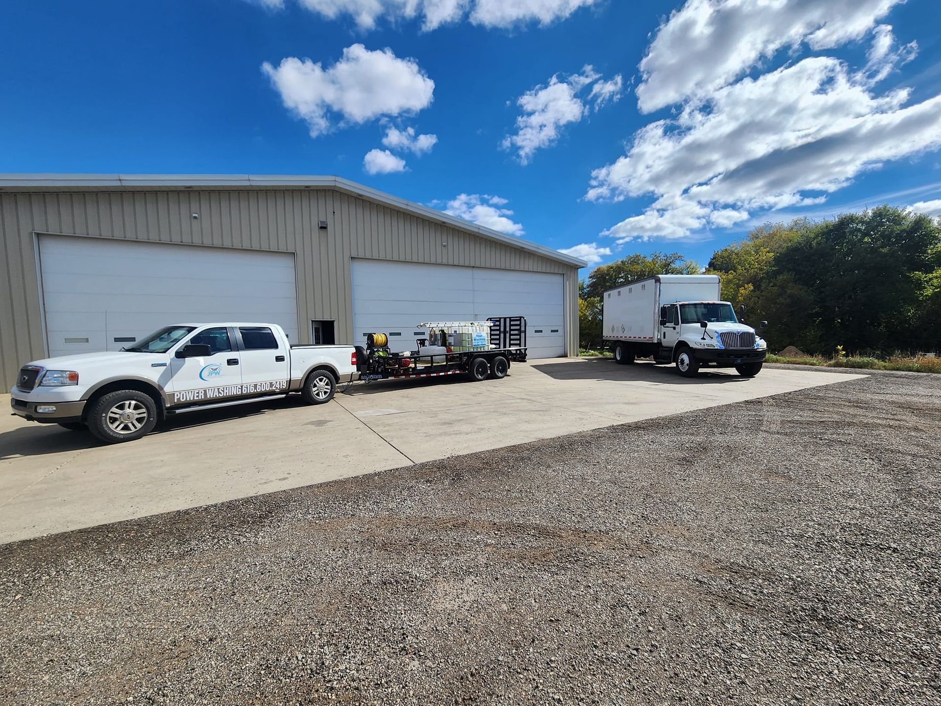 White trucks parked in front of a tan industrial building under a blue sky with fluffy clouds.