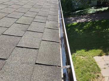 Overhead view of a roof with gray shingles and a gutter, beside green grass.