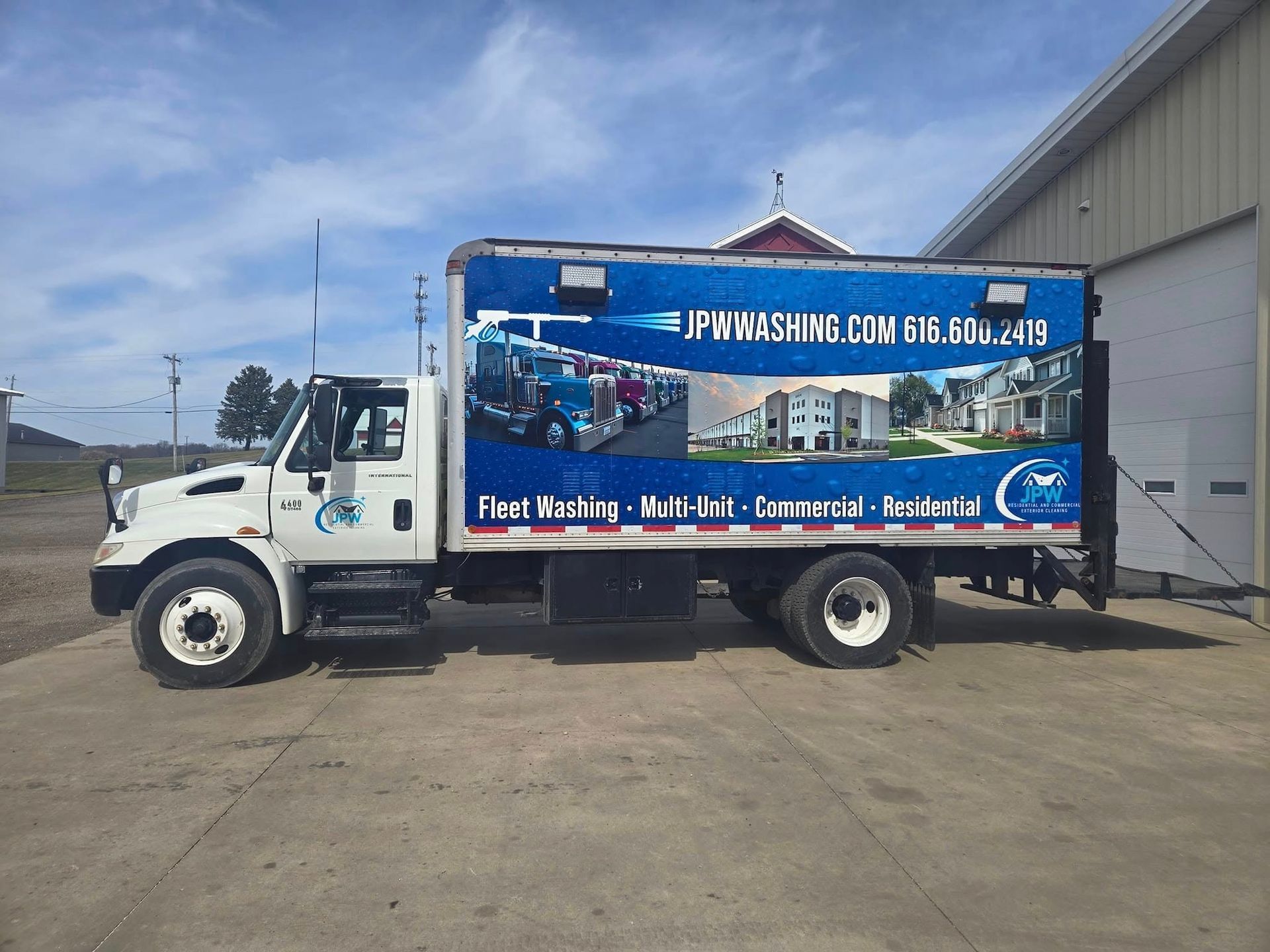 White truck with blue advertisement for PA washing, parked outside building on a sunny day.