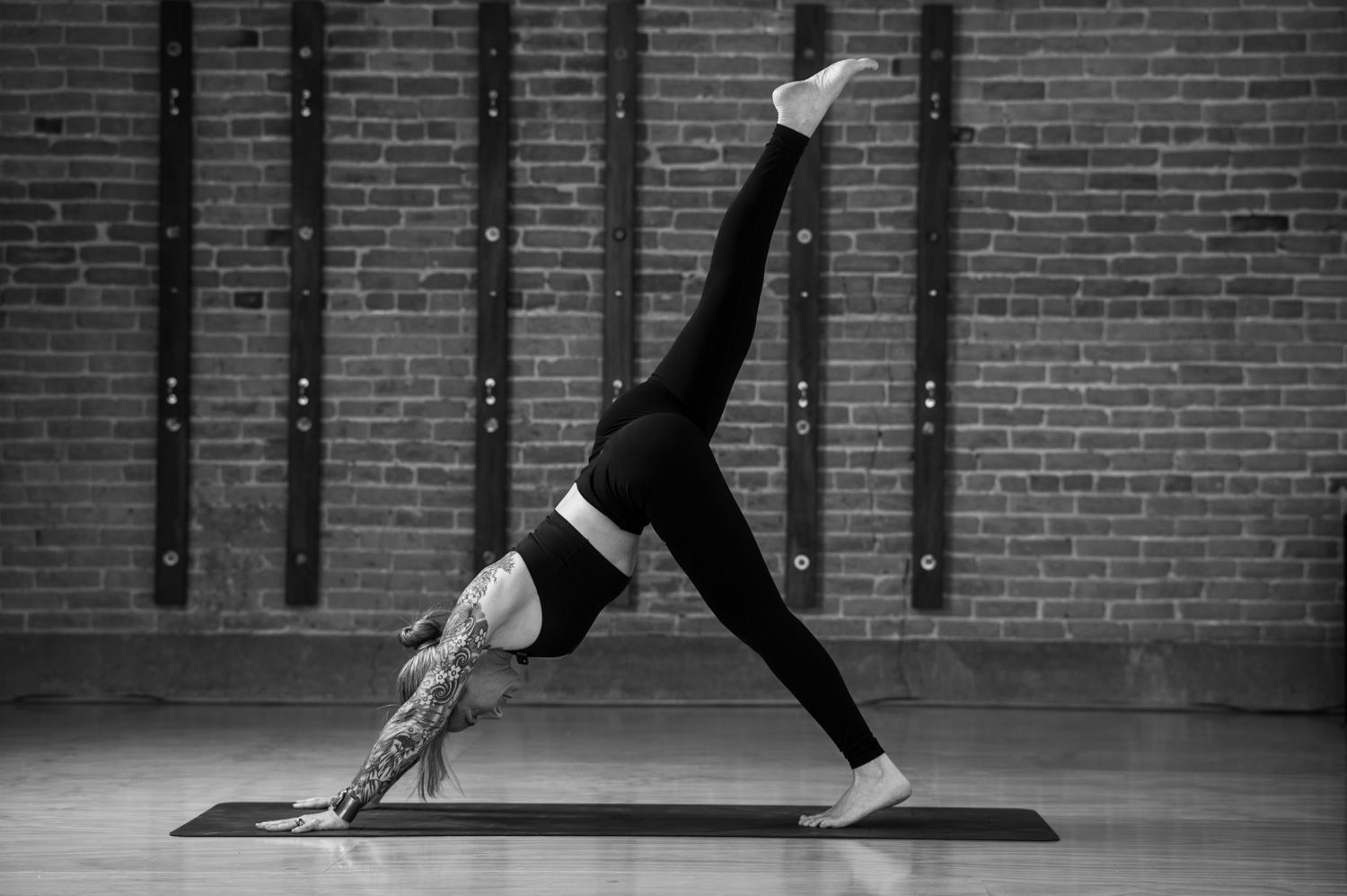 A woman is doing yoga on a mat in front of a brick wall.